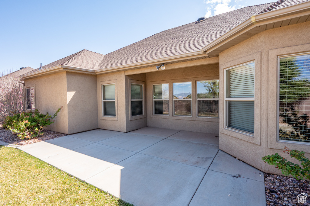 Back of property featuring a shingled roof, stucco siding, and a patio area