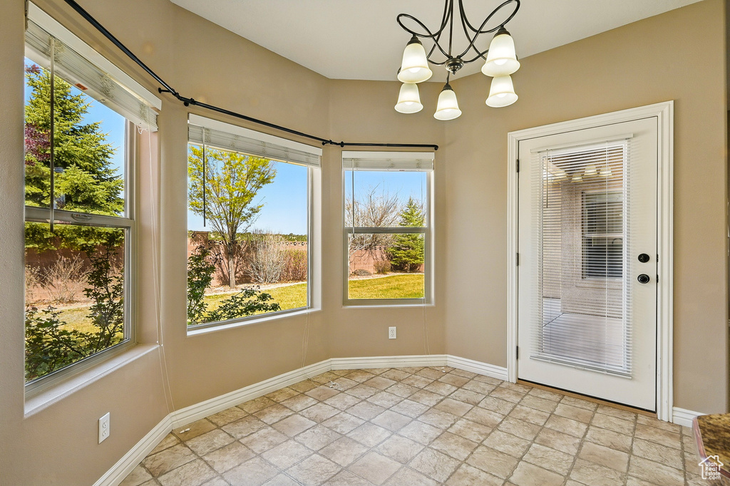 Unfurnished dining area featuring baseboards, stone tile flooring, and a notable chandelier