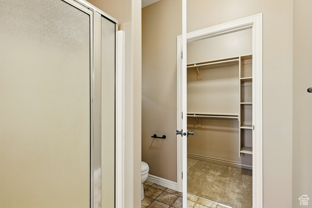 Bathroom with a walk in closet, baseboards, a stall shower, and toilet