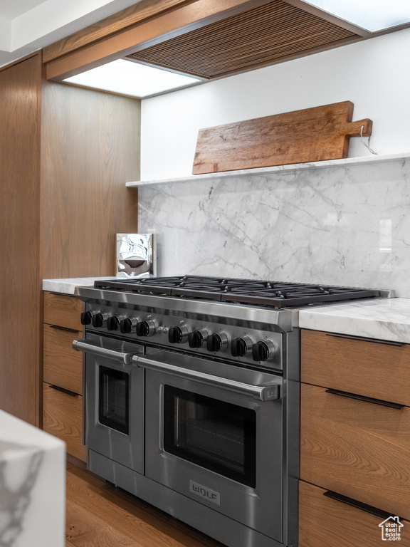 Kitchen featuring tasteful backsplash, brown cabinets, light countertops, premium range hood, and range with two ovens