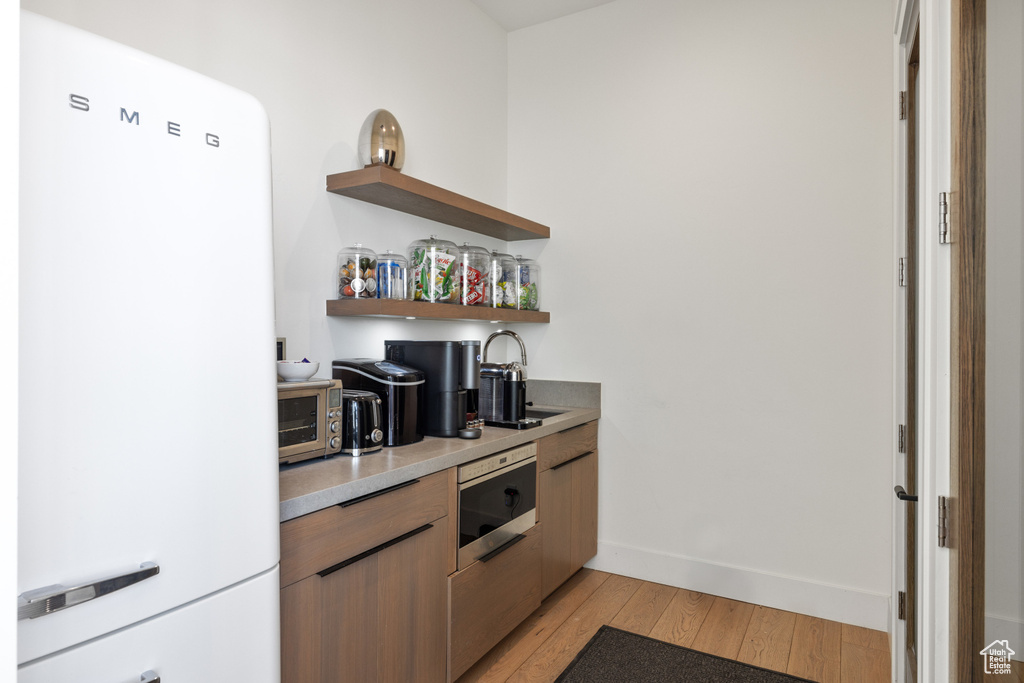 Kitchen featuring light wood finished floors, a sink, freestanding refrigerator, open shelves, and light countertops