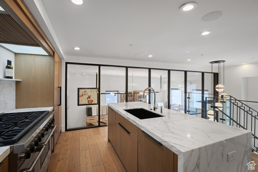 Kitchen featuring recessed lighting, a sink, a center island with sink, range with two ovens, and light wood-style flooring