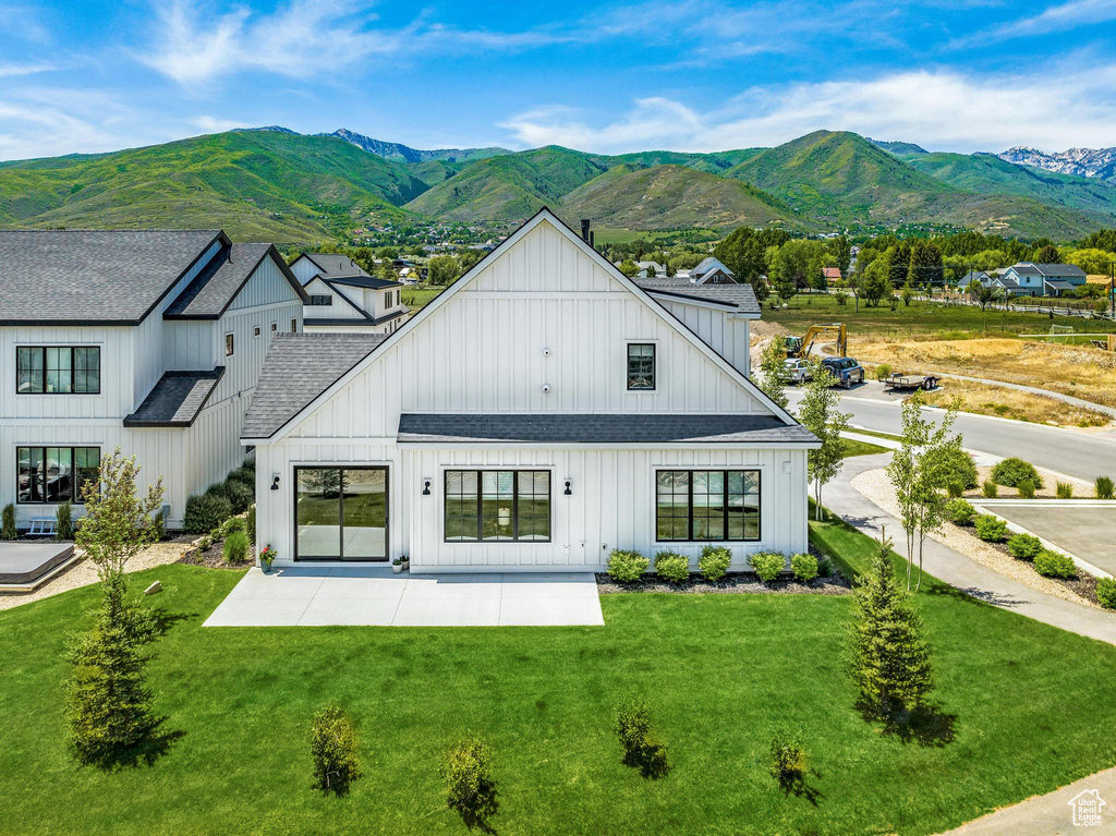 Back of property with a lawn, a mountain view, a shingled roof, and a patio area