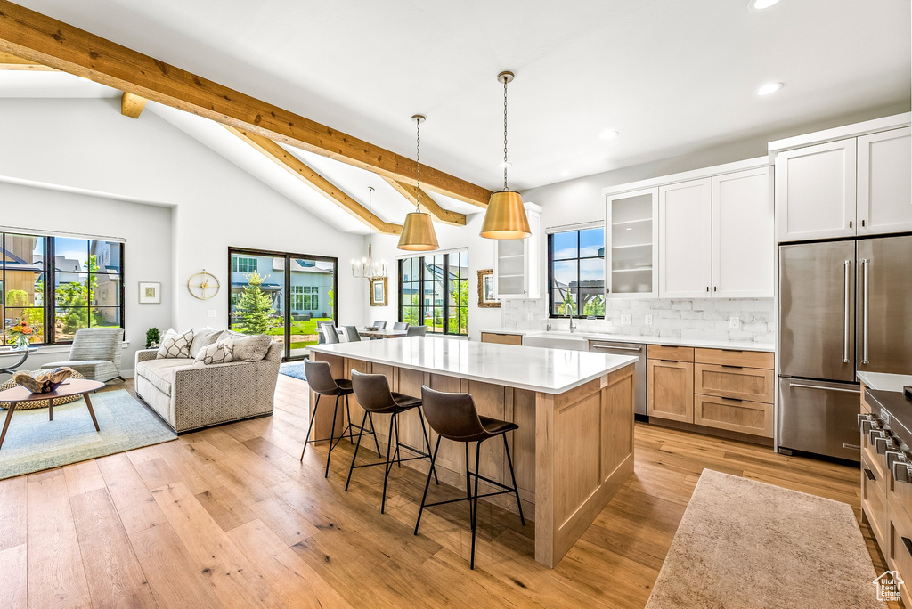 Kitchen with beam ceiling, glass insert cabinets, a center island, recessed lighting, and stainless steel appliances