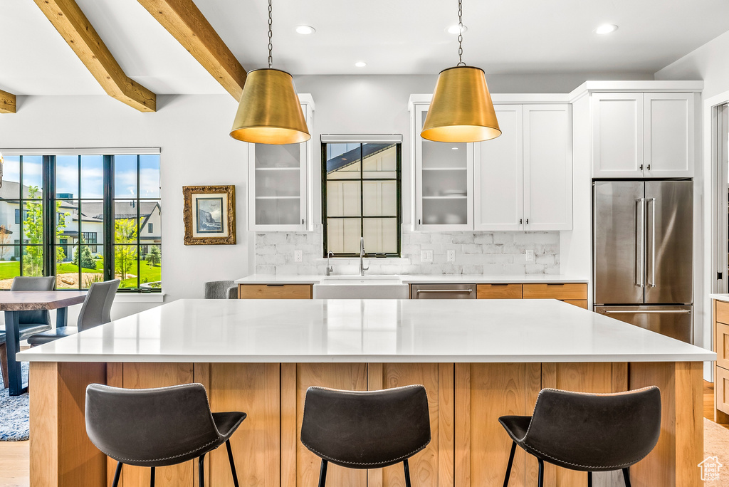 Kitchen with beamed ceiling, glass insert cabinets, a sink, appliances with stainless steel finishes, and backsplash