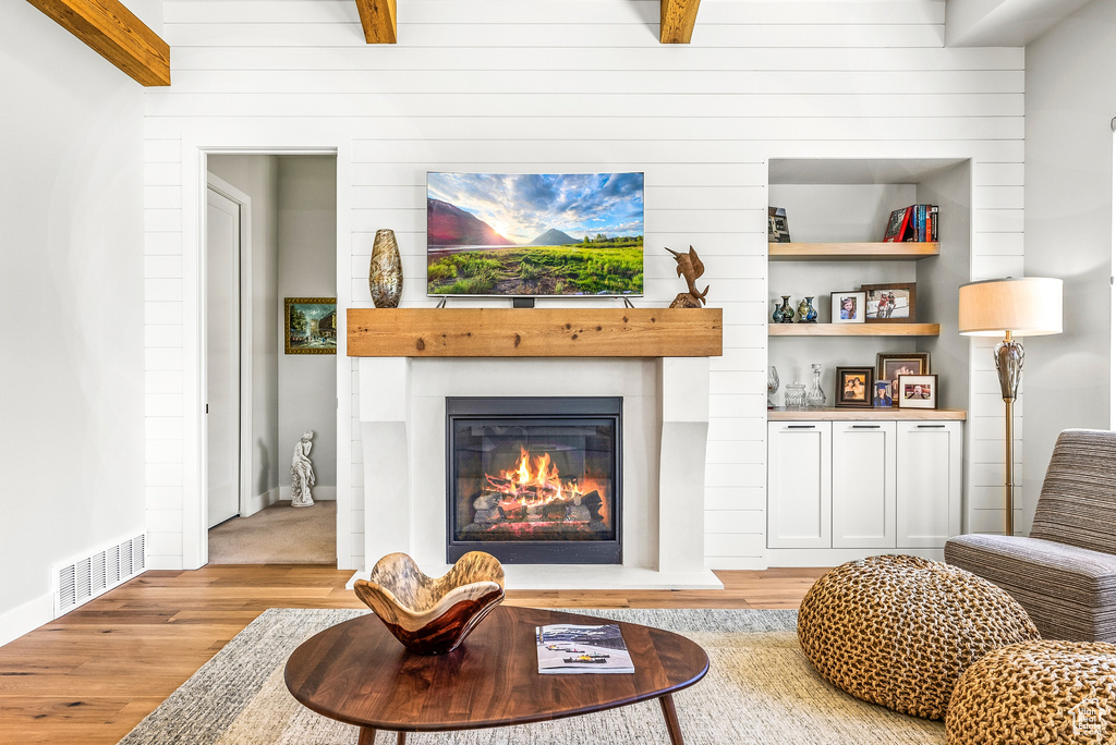 Living room featuring a glass covered fireplace, beamed ceiling, light wood-type flooring, and visible vents