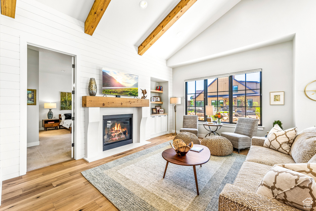 Living room featuring a glass covered fireplace, wood finished floors, beam ceiling, high vaulted ceiling, and built in shelves