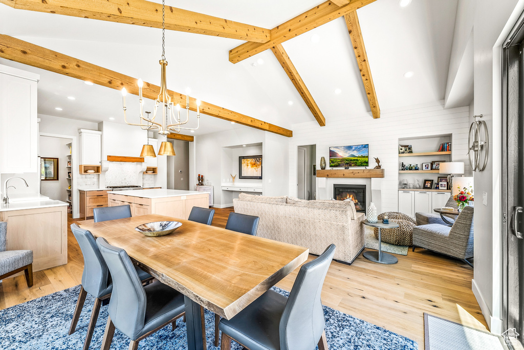 Dining room with a warm lit fireplace, an inviting chandelier, light wood-style flooring, recessed lighting, and vaulted ceiling with beams
