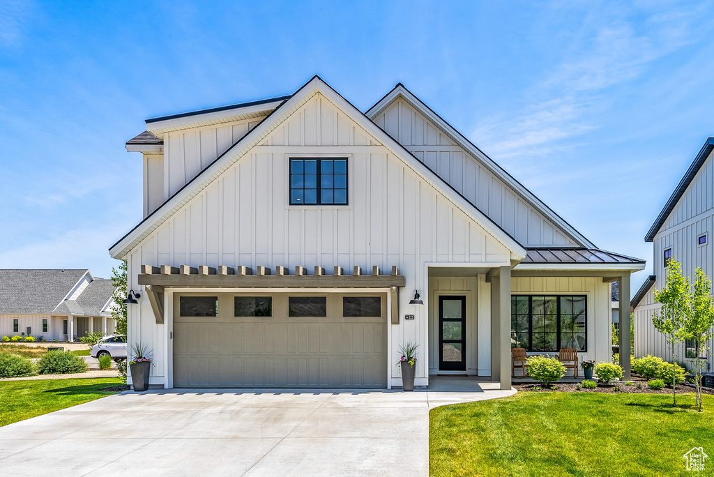 Modern farmhouse featuring board and batten siding, a standing seam roof, driveway, and a front yard