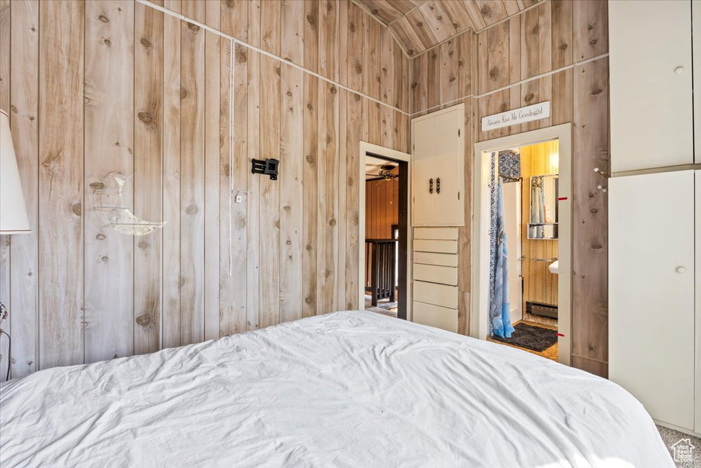Bedroom featuring wood walls, ensuite bathroom, and lofted ceiling