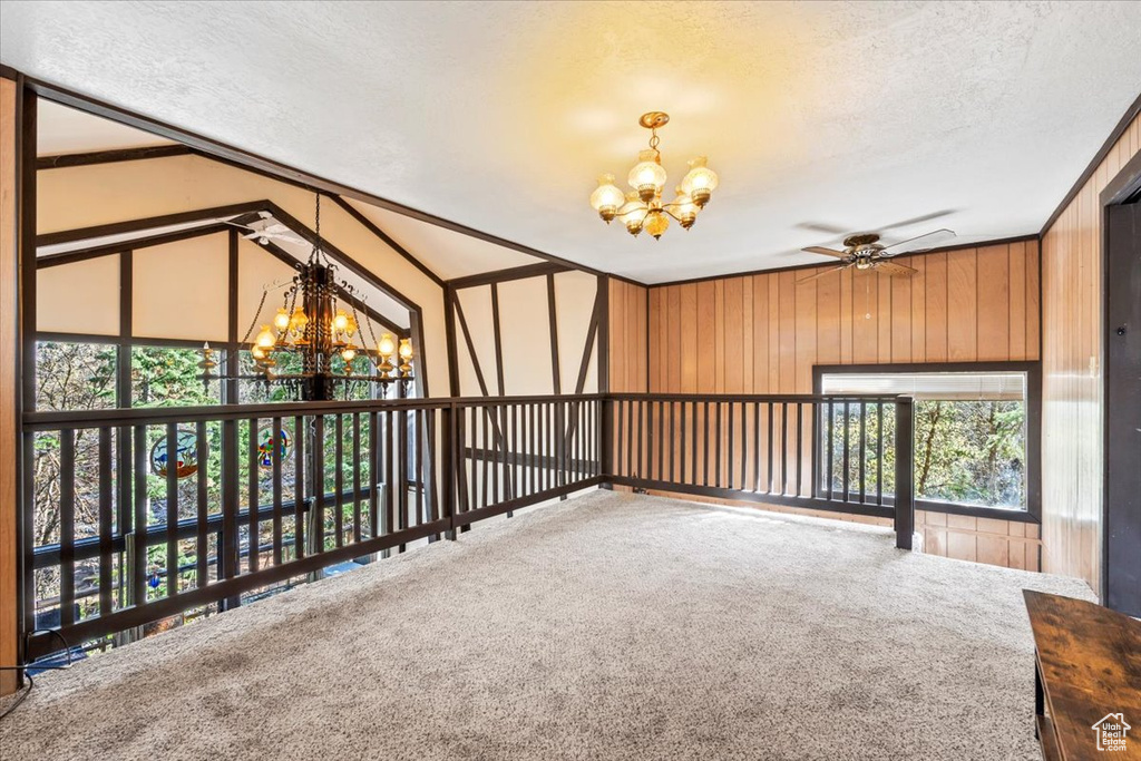 Unfurnished room featuring ceiling fan with notable chandelier, carpet flooring, wood walls, and a textured ceiling