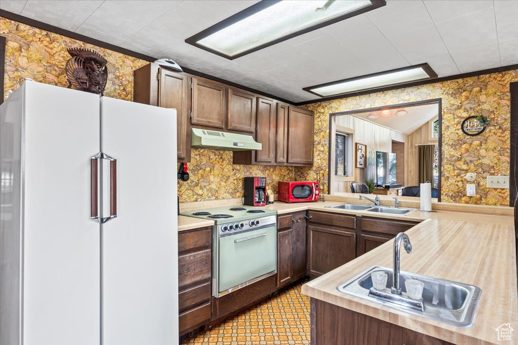 Kitchen with a sink, white appliances, light countertops, wallpapered walls, and under cabinet range hood