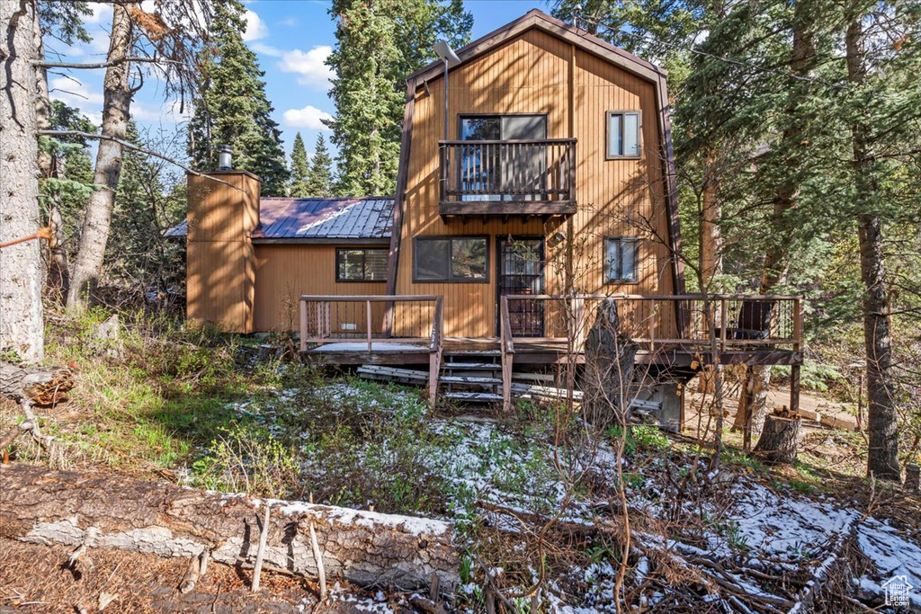Rear view of property with a deck, metal roof, a balcony, and a chimney