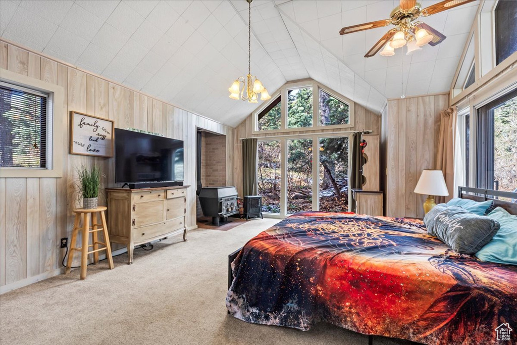 Bedroom featuring a wood stove, lofted ceiling, wooden walls, a chandelier, and carpet