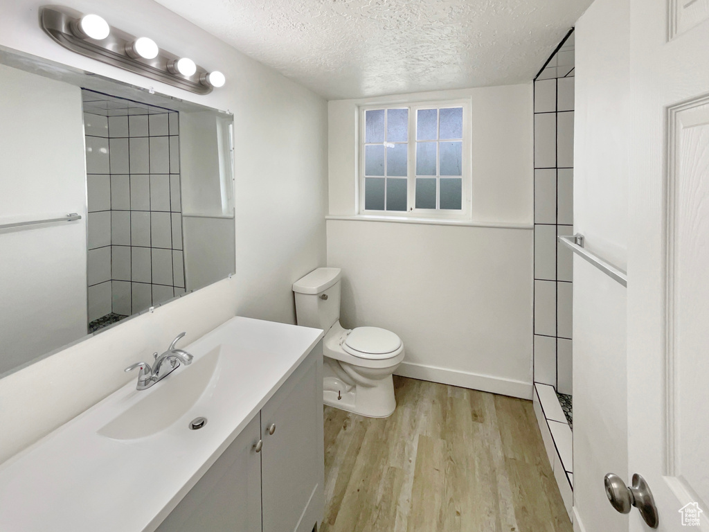 Full bath with vanity, toilet, a textured ceiling, wood finished floors, and tiled shower