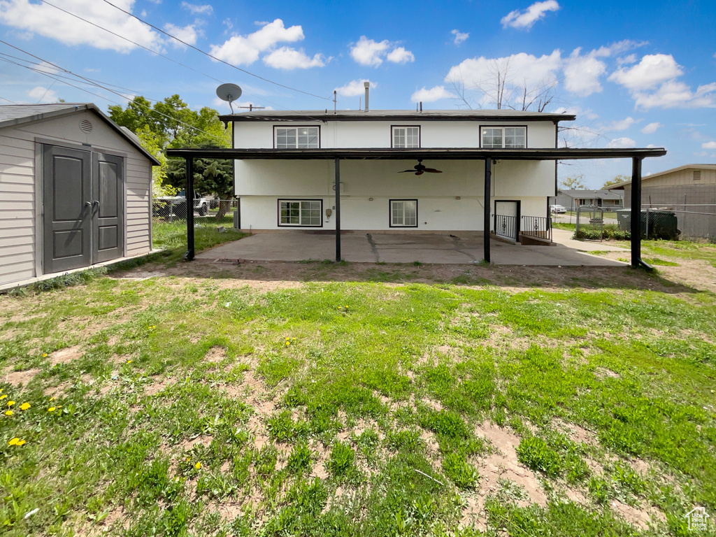 Rear view of house featuring ceiling fan, fence, a storage unit, a yard, and a patio