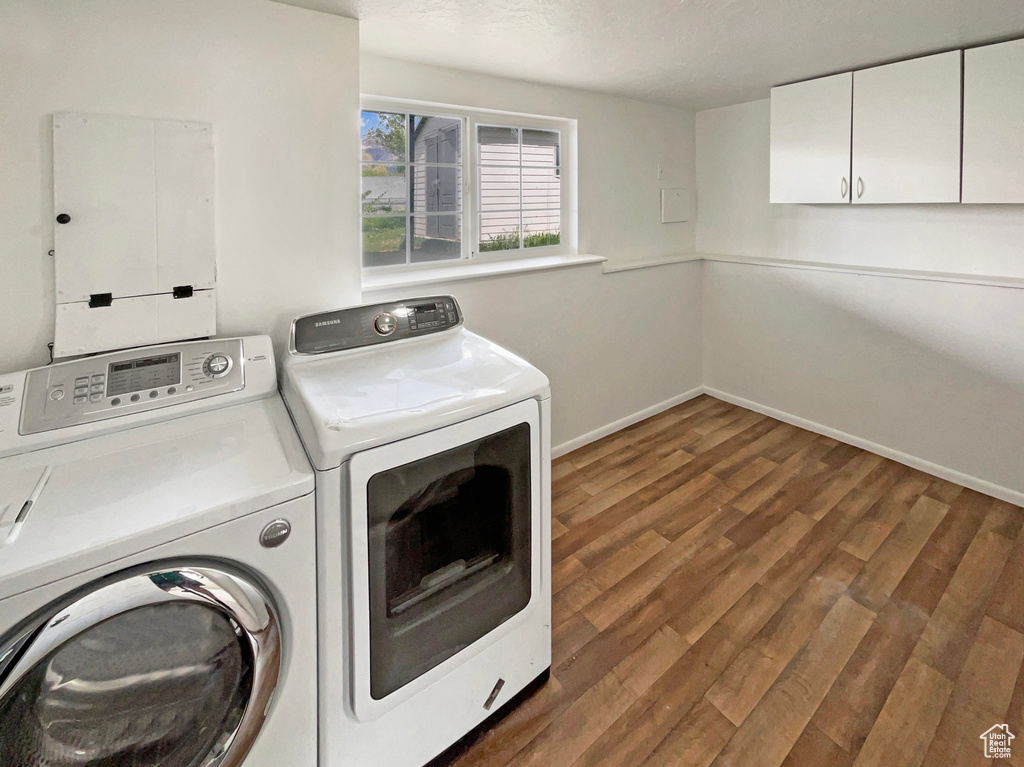 Washroom with baseboards, cabinet space, wood finished floors, and washing machine and clothes dryer