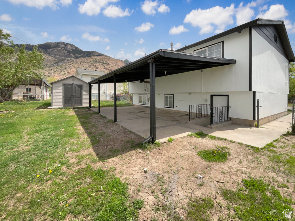 Back of property with a shed, a patio area, a lawn, a mountain view, and an outbuilding