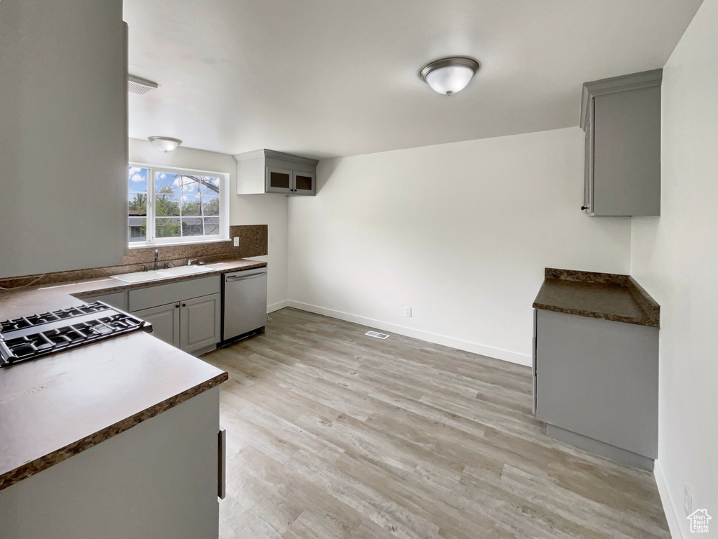 Kitchen with stainless steel dishwasher, stovetop, a sink, light wood finished floors, and gray cabinetry