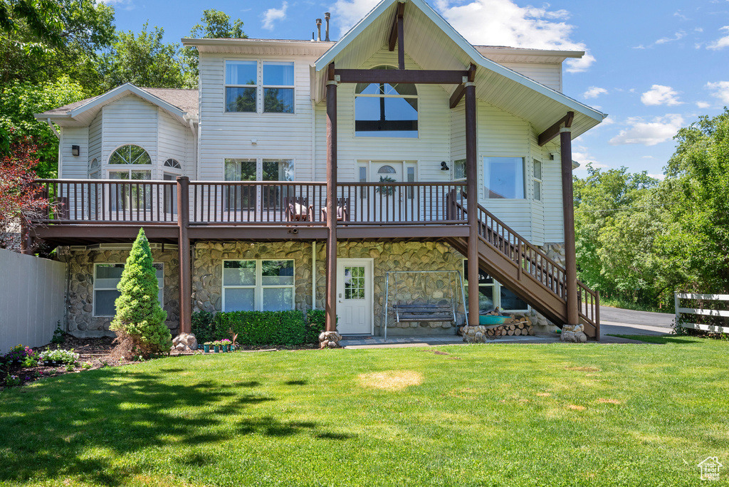 Rear view of property featuring a deck, a lawn, stone siding, and stairway