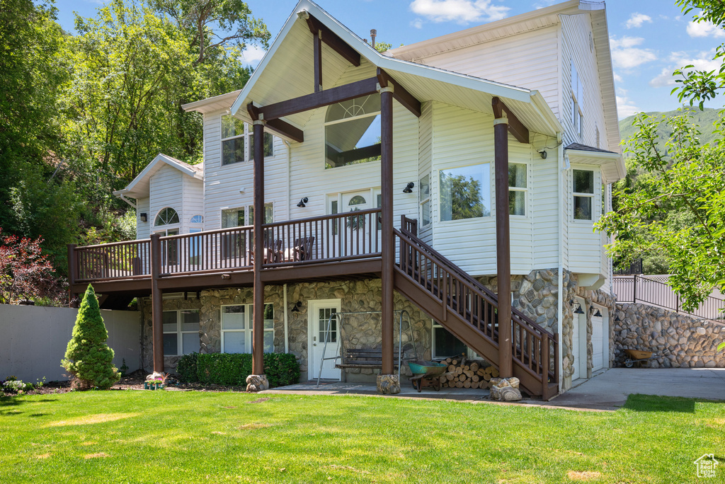 Back of house featuring a lawn, a wooden deck, stone siding, stairway, and a garage