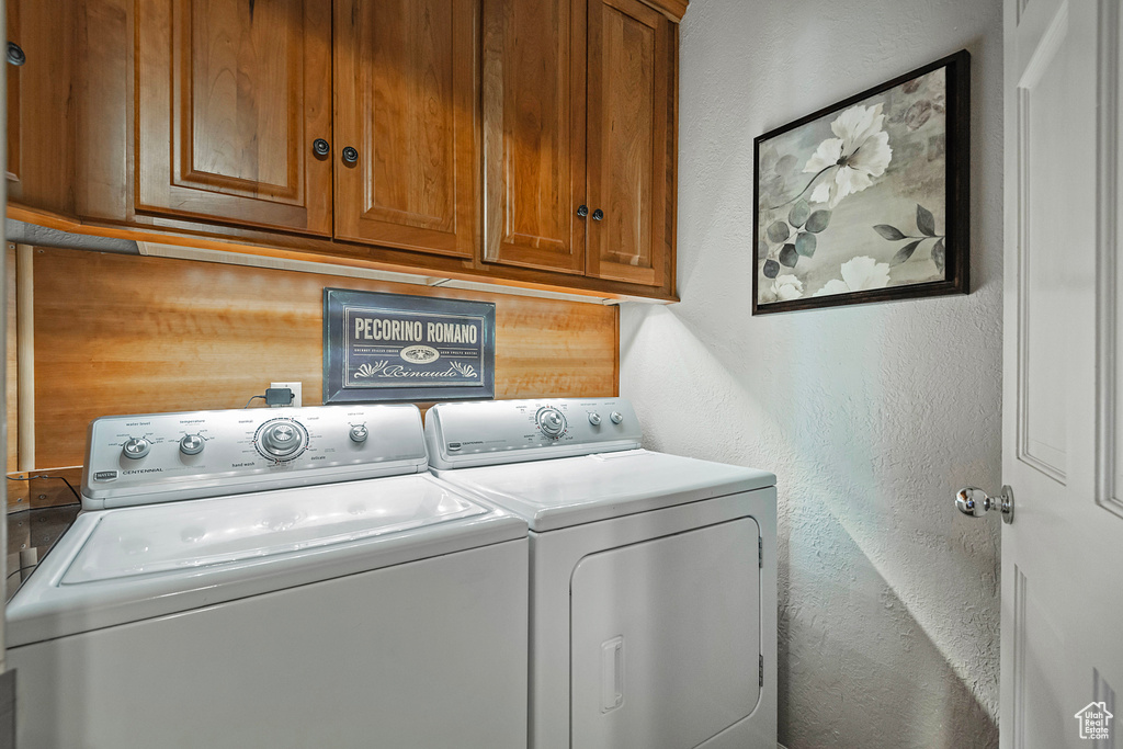 Washroom featuring a textured wall, washer and clothes dryer, and cabinet space