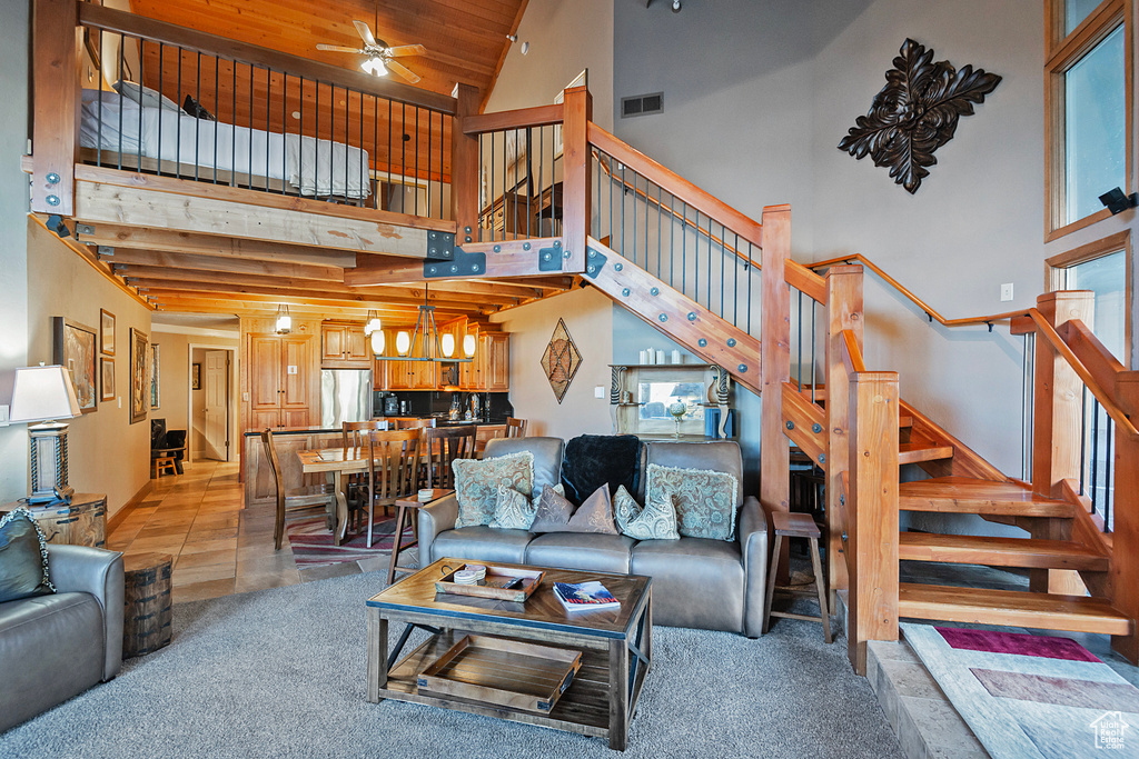 Living area with stairs, a high ceiling, ceiling fan with notable chandelier, light colored carpet, and visible vents