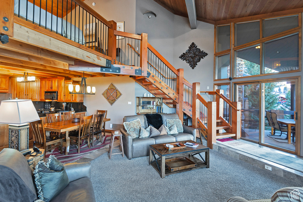 Carpeted living room featuring stairway, wooden ceiling, a chandelier, a high ceiling, and beam ceiling