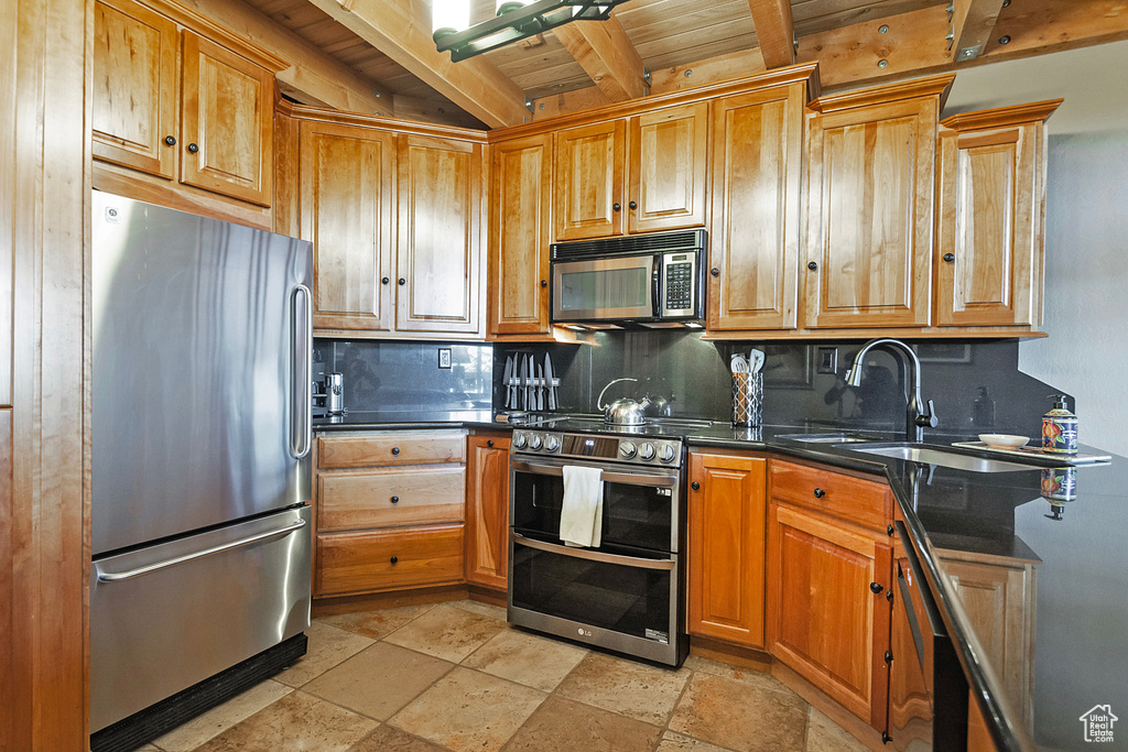 Kitchen with stone tile floors, backsplash, dark countertops, beam ceiling, and appliances with stainless steel finishes