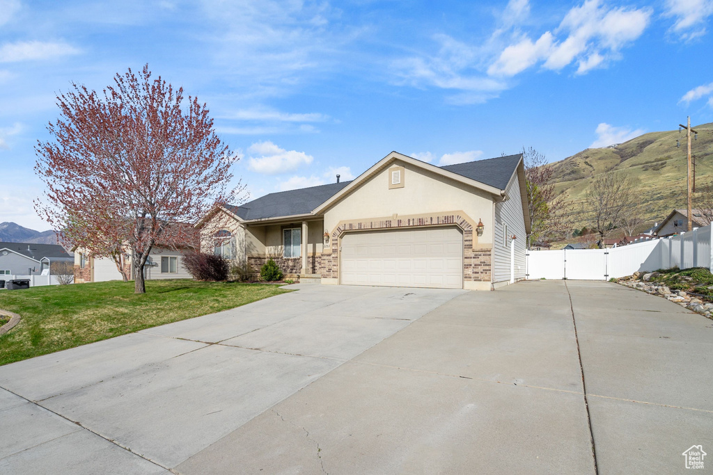 Ranch-style home with a front lawn, driveway, fence, a mountain view, and a garage