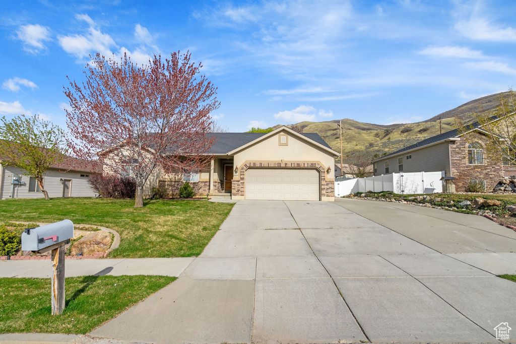 Ranch-style home featuring driveway, an attached garage, fence, a mountain view, and a front yard