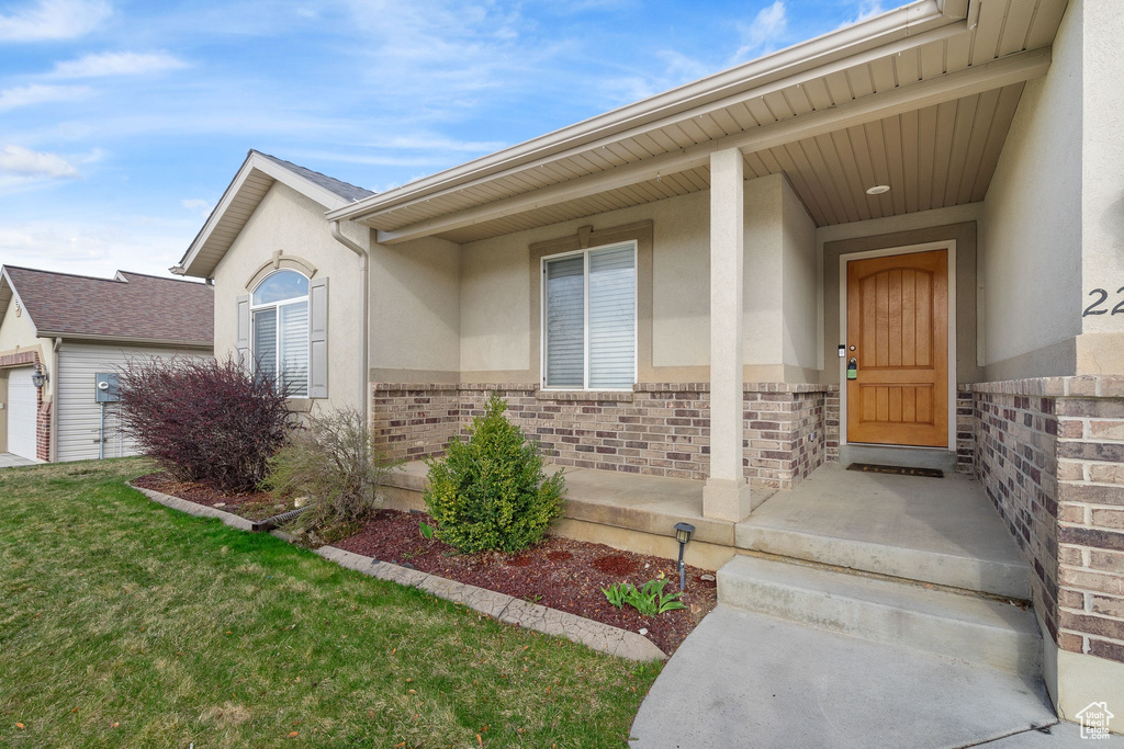 Doorway to property with brick siding, a lawn, and stucco siding