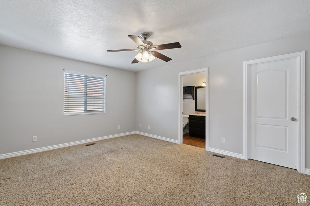 Unfurnished bedroom with visible vents, connected bathroom, baseboards, carpet flooring, and ceiling fan
