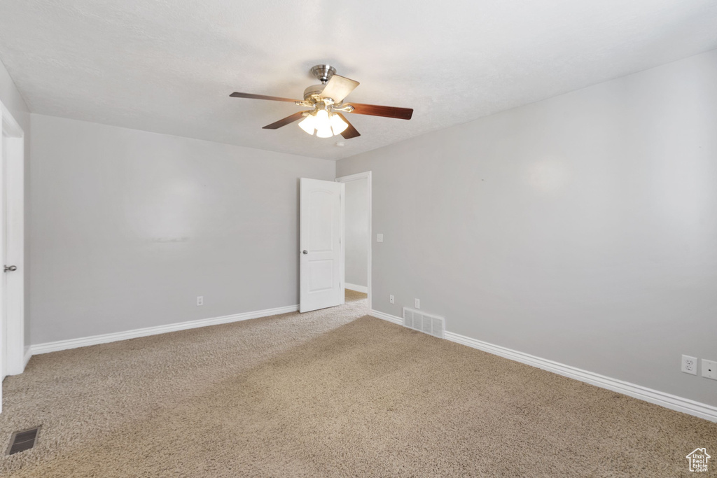 Empty room featuring carpet floors, visible vents, baseboards, and ceiling fan