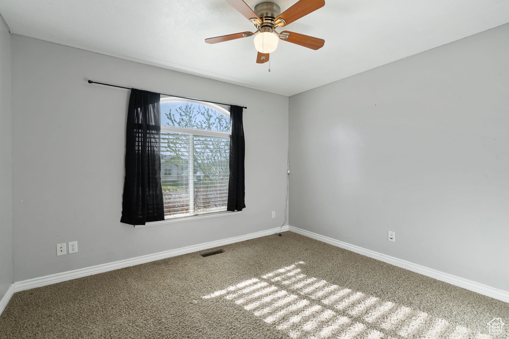 Carpeted spare room with visible vents, a ceiling fan, and baseboards