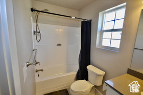 Bathroom featuring baseboards, shower / bathtub combination with curtain, toilet, and vanity