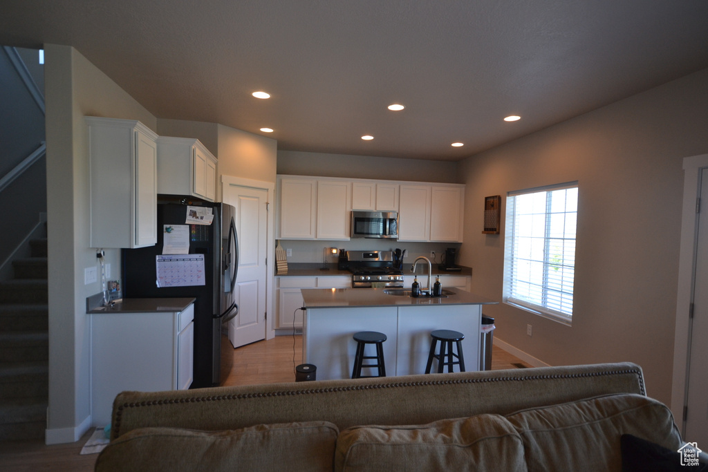 Kitchen with appliances with stainless steel finishes, a sink, dark countertops, light wood finished floors, and recessed lighting