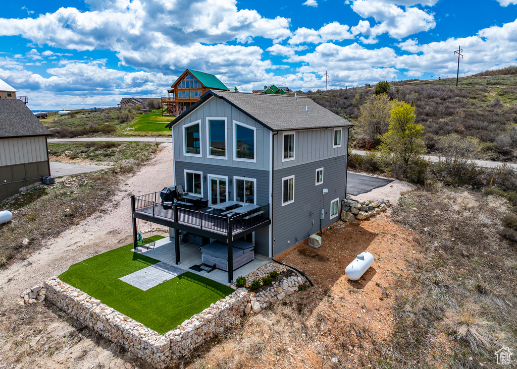 Rear view of house featuring a deck, roof with shingles, a patio area, board and batten siding, and a yard