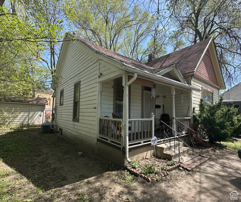 View of front of property with a shingled roof, central AC, covered porch, and a chimney