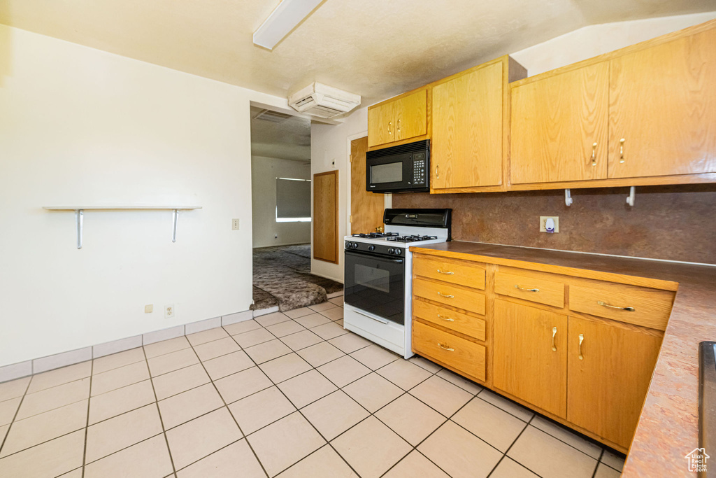 Kitchen featuring light tile patterned flooring, black microwave, and white gas range