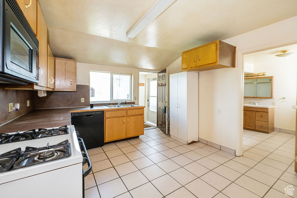 Kitchen with a sink, black appliances, light tile patterned flooring, and lofted ceiling