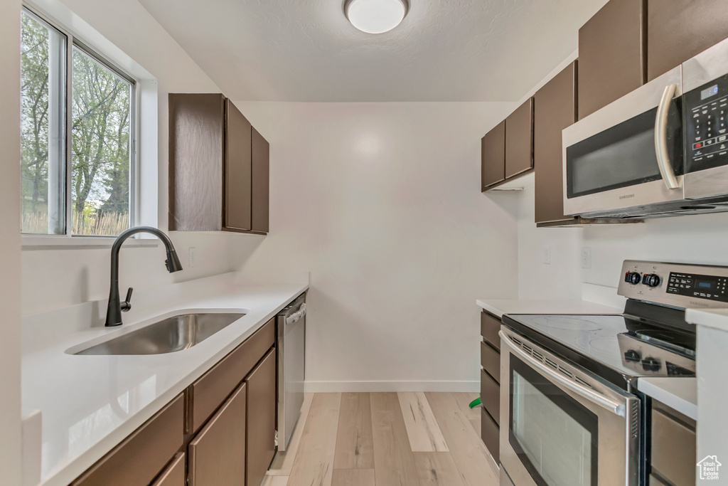 Kitchen featuring a sink, stainless steel appliances, light wood-type flooring, baseboards, and light countertops