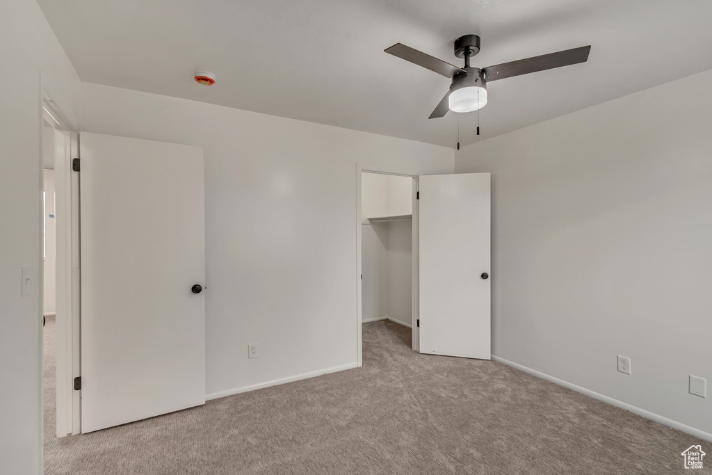 Unfurnished bedroom with a walk in closet, ceiling fan, light colored carpet, and baseboards