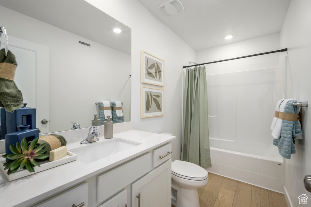 Bathroom with vanity, visible vents, wood finished floors, shower / bath combination with curtain, and toilet