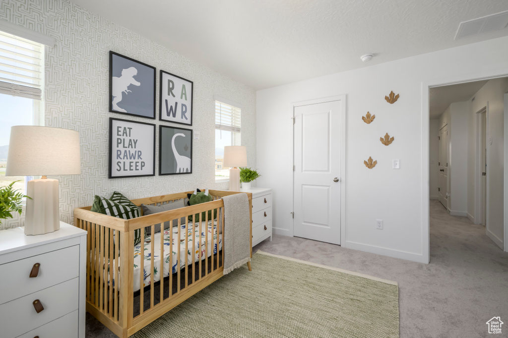 Bedroom with a nursery area, baseboards, visible vents, and light carpet