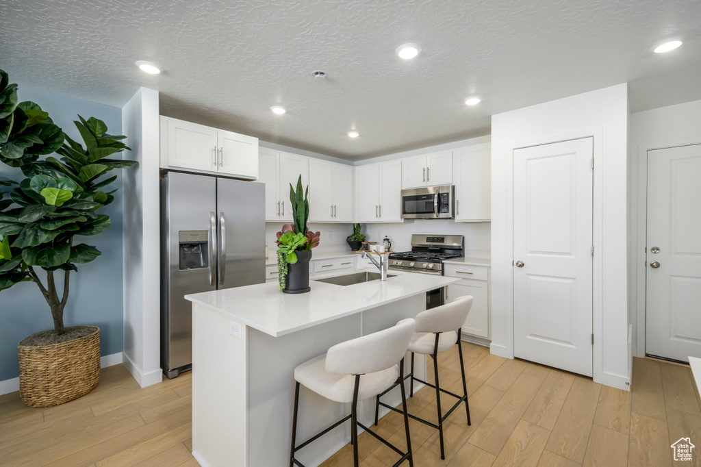 Kitchen featuring a breakfast bar, a sink, light wood-style flooring, stainless steel appliances, and white cabinetry