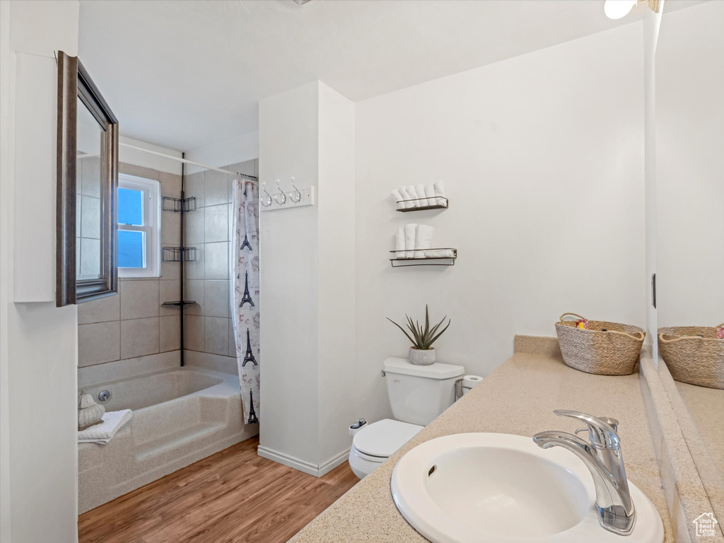 Full bathroom featuring wood finished floors, baseboards, vanity, toilet, and shower / bathtub combination with curtain