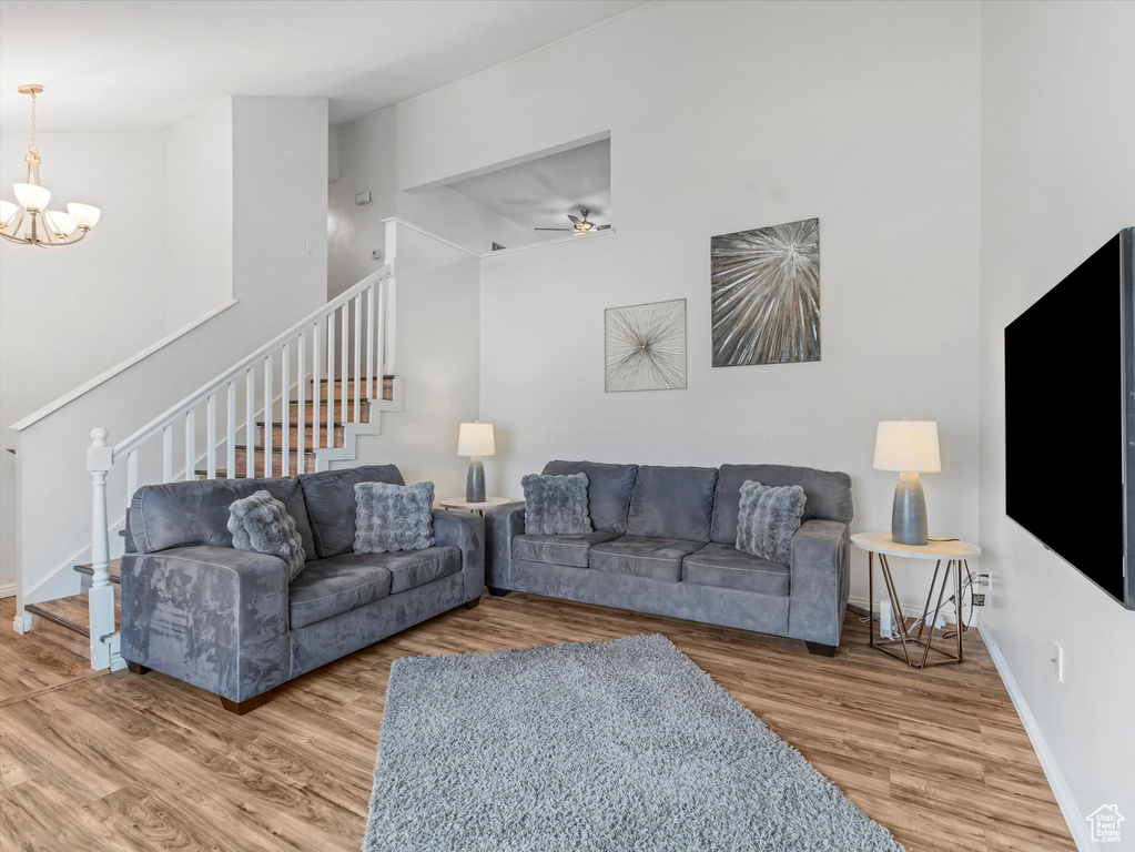 Living room featuring baseboards, ceiling fan with notable chandelier, wood finished floors, and stairway