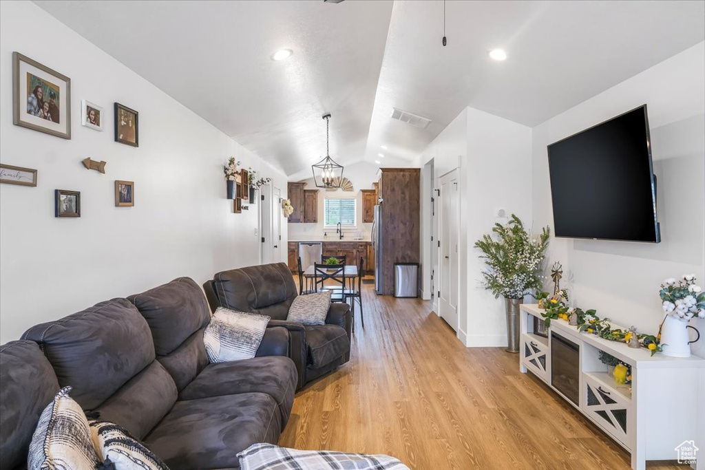 Living room with a chandelier, visible vents, light wood-type flooring, baseboards, and lofted ceiling