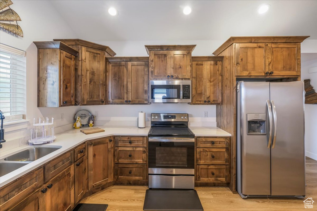 Kitchen featuring light wood-type flooring, a sink, appliances with stainless steel finishes, and light countertops